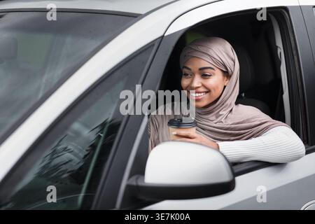 Smiling Black woman in hijab driving car in city during daytime Stock Photo