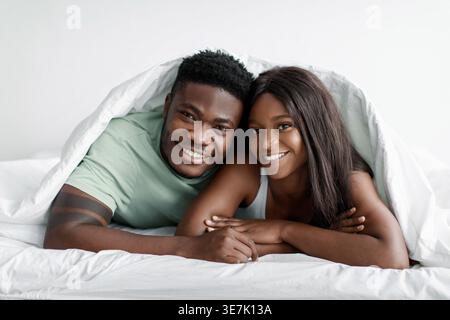 Black couple under bed sheet lying down on bed in bedroom at home Stock Photo