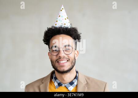 Mixed-race man wearing birthday cap and coat standing against gray background in studio Stock Photo