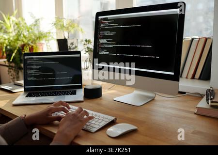 Black female programmer in hijab working codes on computer while sitting at table at home office Stock Photo