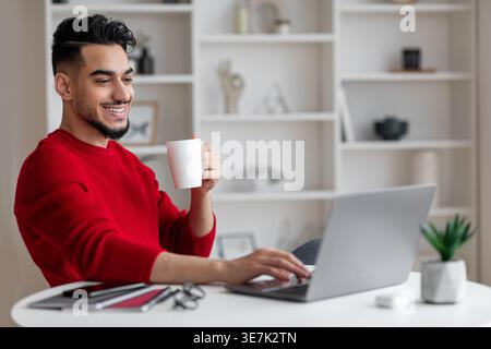 Arab man having coffee typing on laptop sitting at desk at home Stock Photo