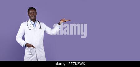 Smiling Black male doctor with dreads wearing white suit with stethoscope showing aside while standing against purple background in studio Stock Photo