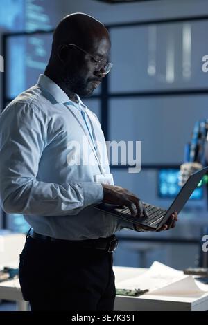 Black male computer engineer with eyeglasses using laptop while standing sideways in laboratory Stock Photo