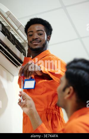Indian male technician giving screwdriver to Black male coworker while standing in house of customer Stock Photo