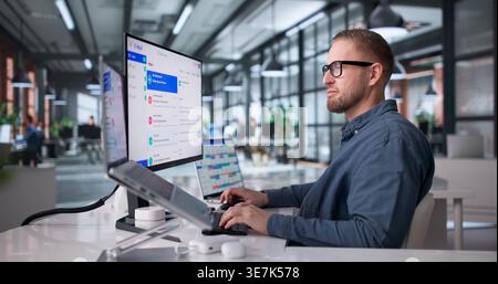 Man Focused On Reviewing Emails On Desktop Computer In A Compact Office Setting Stock Photo