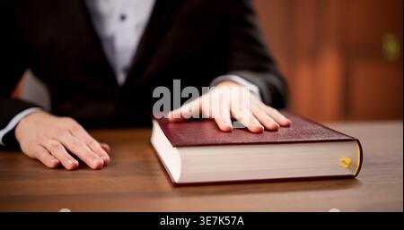 Young Man Takes Formal Oath In Courtroom, Hand Resting On Book Before Testifying Stock Photo