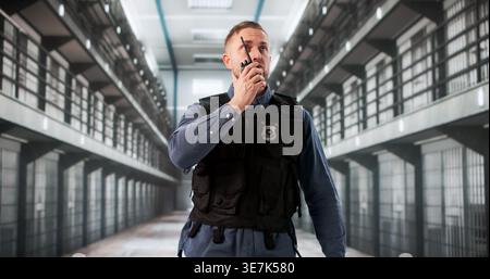 Prison Officer Patrols Hallway, Communicating Rapidly Via Walkie Talkie Stock Photo