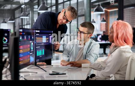 Cybersecurity Engineer Analyzes Data On Screen While Collaborating With Diverse Team. Stock Photo