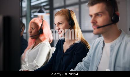Customer Support Agent Smiles While Talking On Headset At Desk. Stock Photo