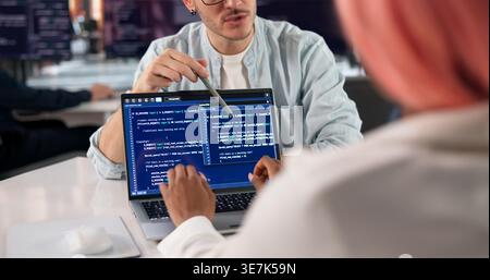 Software Engineer Writes Code On Laptop While Discussing Project With Team. Stock Photo
