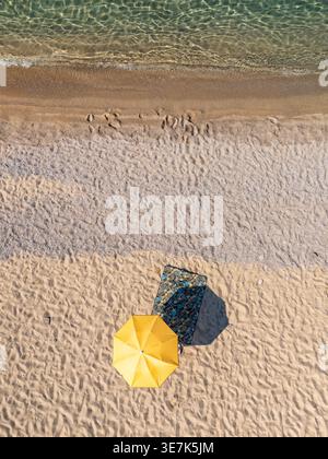 Aerial top down view of a yellow sun umbrella on an empty white sand beach Stock Photo
