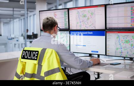 Police Officer Focused On Desktop Computer Conducting Background Verification In Modern Office Setting Stock Photo