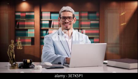 Cheerful Hispanic Male Attorney In Office Surrounded By Legal Books, Smiling Confidently At Camera Stock Photo
