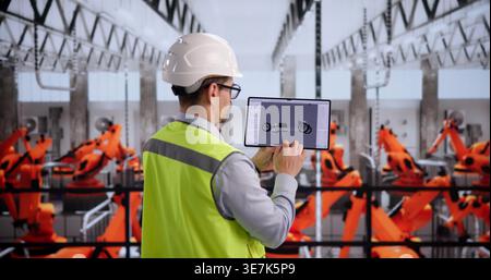Automotive Technician Reviews Auto Components With Tablet Device In Manufacturing Plant Stock Photo