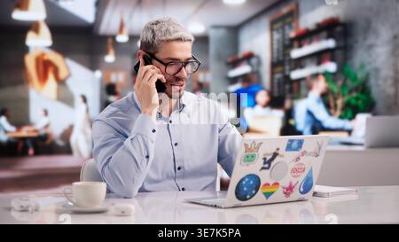 Creative Graphic Designer Collaborating With Client Over Phone While Crafting Web Art On Laptop Stock Photo