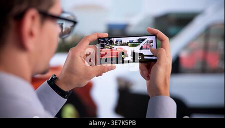 Insurance Agent Examines Vehicle Damage After Crash Using Smartphone Stock Photo