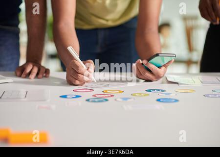 Group of Asian male designers holding smartphone leaning on table working together in office during daytime Stock Photo