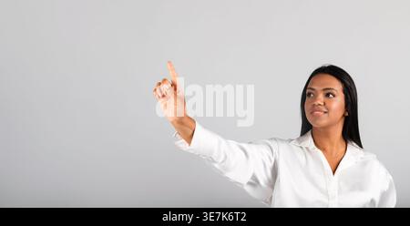 Black business woman looking and pointing finger away standing against gray background in studio Stock Photo