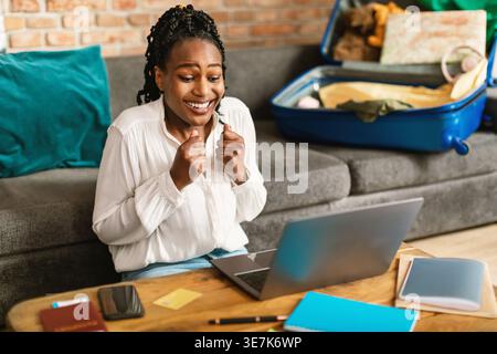Black woman with twists and hands near body looking at laptop sitting at table in living room at home Stock Photo