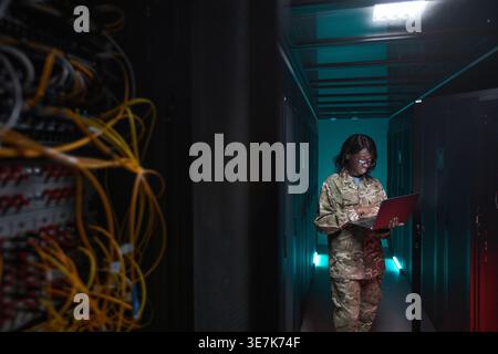 Black female soldier wearing eyeglasses using laptop while standing in server room Stock Photo