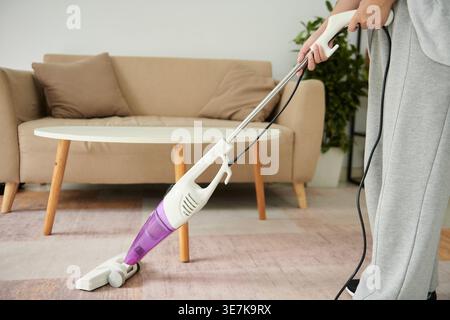 Asian woman cleaning carpet using vacuum cleaner standing near table in living room at home Stock Photo