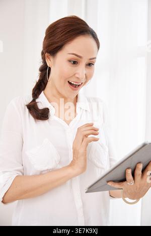 Surprised Asian woman using tablet while standing at home Stock Photo