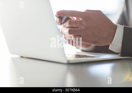 Chinese businessman using smartphone while sitting at table with laptop in office Stock Photo