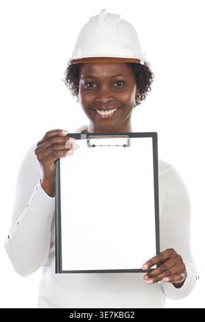 Smiling Black female engineer wearing hard hat holding clipboard standing  against white background Stock Photo