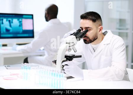 Middle eastern man looking through microscope with Black man coworker using computer in laboratory Stock Photo