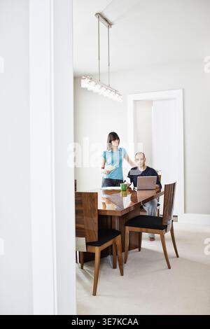 Black, Middle Eastern man sitting working on laptop with wife at home Stock Photo