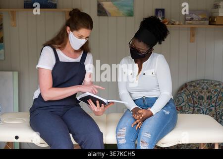 Black woman sitting with therapist reading book during therapy session at home Stock Photo