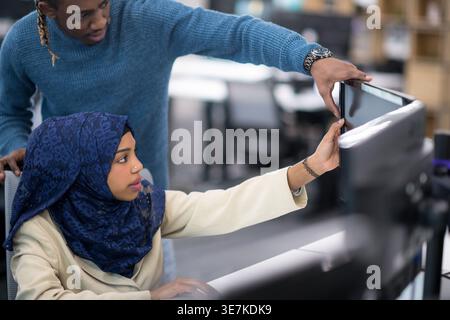 Focused Black man using computer standing behind Black muslim female coworker sitting during meeting in office Stock Photo