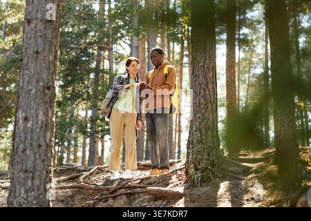 Black man with caucasian female friend using mobile phone together while standing on hill in the forest Stock Photo
