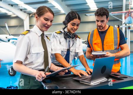 Middle Eastern female pilot with her team using laptop for airplane checkup in hangar Stock Photo