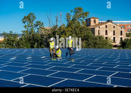 Diverse group of engineers wearing hard hats and safety vests using clipboard, laptop, and tablet while inspecting large solar panel array on build... Stock Photo