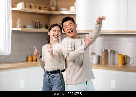 Cheerful Asian couple having fun dancing together in kitchen at home Stock Photo