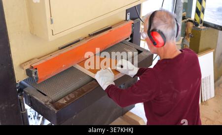 Carpenter sanding wood plank using belt sander machine Stock Photo