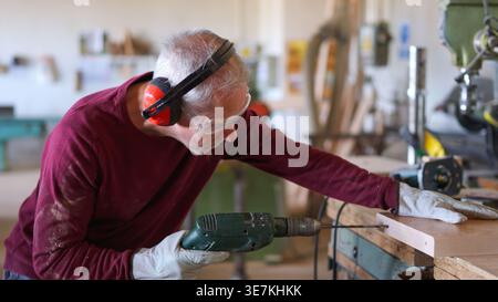 Carpenter drilling wood plank wearing safety equipment Stock Photo