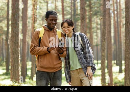 Black man with caucasian female friend using smLifestylephpone while standing together in the forest Stock Photo