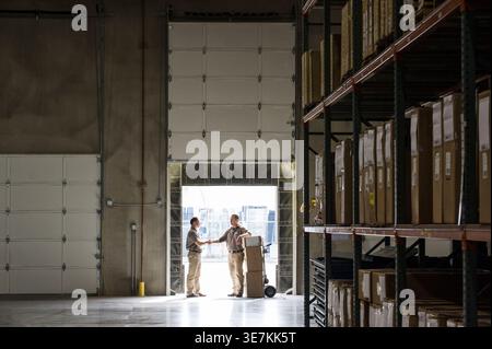 Hispanic and Pacific Islander male workers shaking hands standing in warehouse Stock Photo