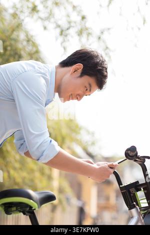 Smiling Chinese man using smartphone scanning QR code to unlock share bike outdoors Stock Photo