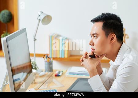 Hands of Asian male graphic designer looking at monitor screen while sitting on chair in office Stock Photo