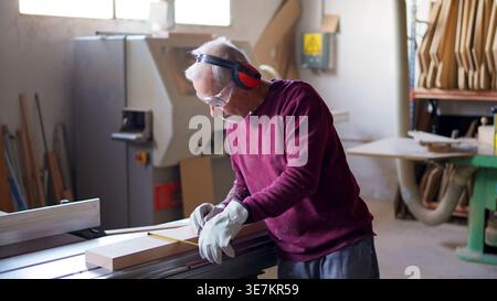 Senior carpenter measuring wood in safety gear with pencil Stock Photo