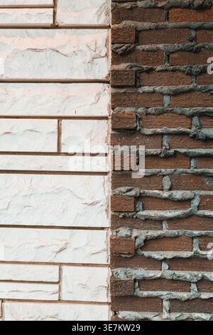 A white wall with a smooth finish stands beside a brown brick wall that has a rough texture. Both surfaces reflect different building styles under nor Stock Photo
