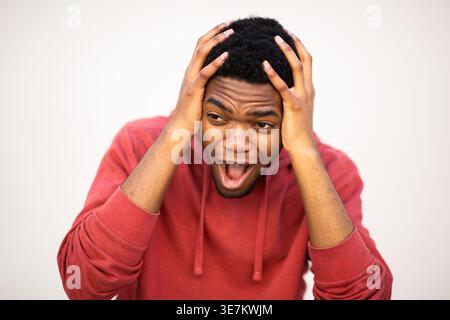 Black male with hands on head and opened mouth standing against white background Stock Photo