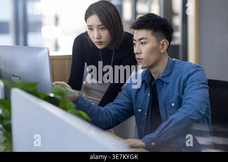 Chinese male and female IT experts working together on computer in office Stock Photo