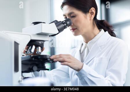Chinese female scientist looking through microscope while working in laboratory Stock Photo