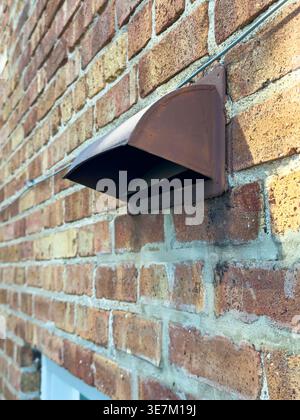 A rusty mailbox is mounted on a brick wall. Sunlight shines on the bricks. The mailbox has an open top and is fixed securely to the wall. Stock Photo