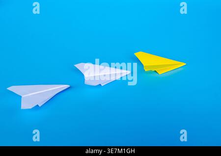 Three paper airplanes in white and yellow moving horizontally across a rich blue field with customizable space for text or ideas Stock Photo