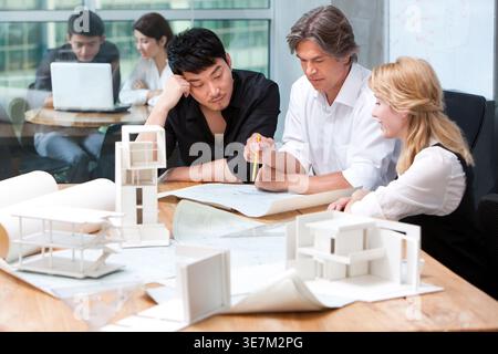 Chinese male architect having a meeting with caucasian male and female architects while sitting at table in office Stock Photo
